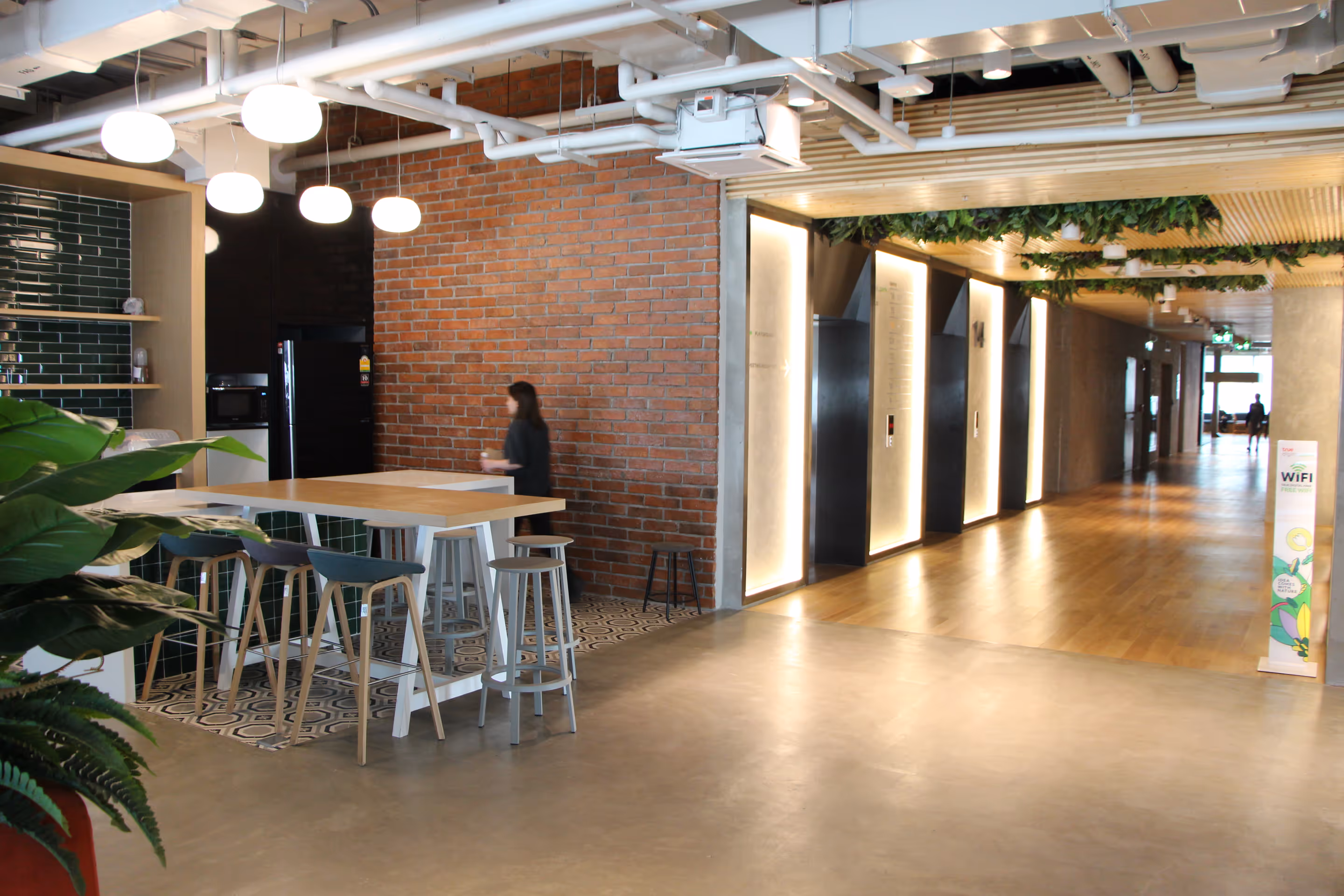 Stylish office space. Brick walls, wooden tables and chairs, and green plants are arranged.