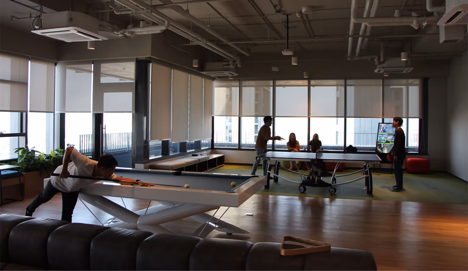 Employees play on the billiard table and ping-pong table in a corner of the spacious office. The view from the window is also open, indicating a comfortable working environment.