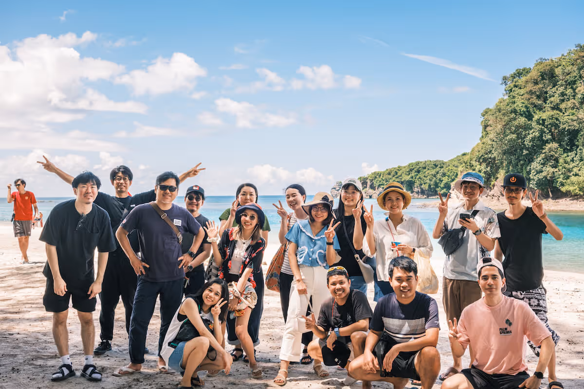 Group photo on the beach. Everyone is doing peace signs and funny poses.