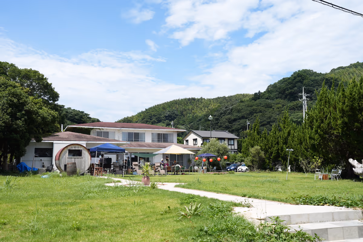 A spacious lawn and white houses standing on it. In the background are a series of green mountains, indicating that this is a place rich in nature.