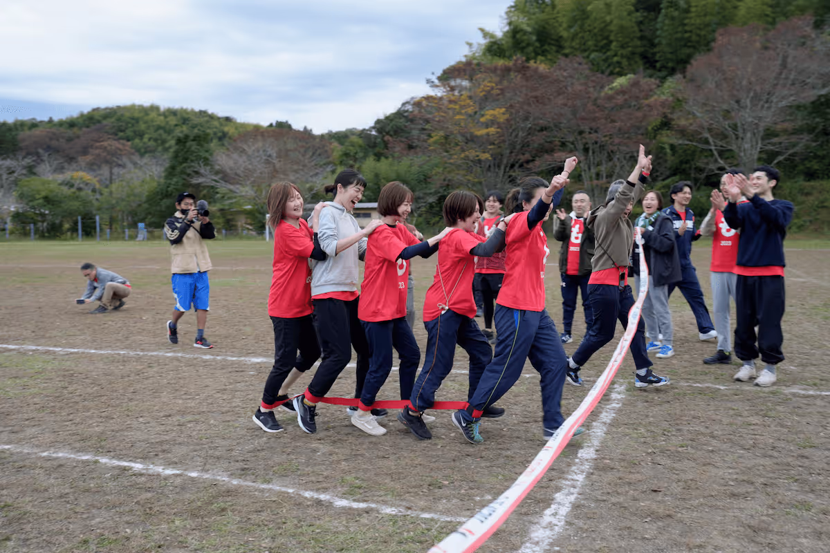 Men and women in red shirts line up and tie their legs together with string, as if they are competing in a mukade race at a field day.