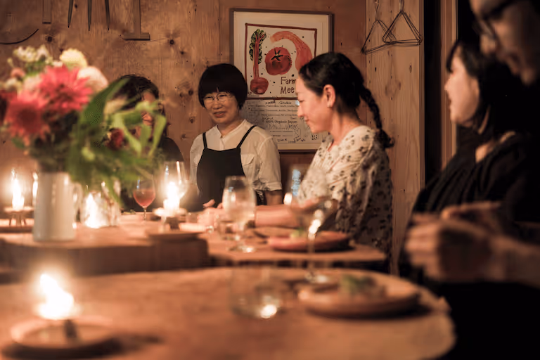 Chef Tomo explains the dishes to the people enjoying the food and wine around a log table.