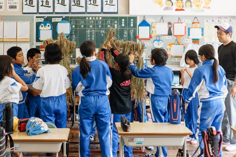In an elementary school classroom, the students are working on a rack for drying rice. They are engaged in the task with a lively and cheerful atmosphere.