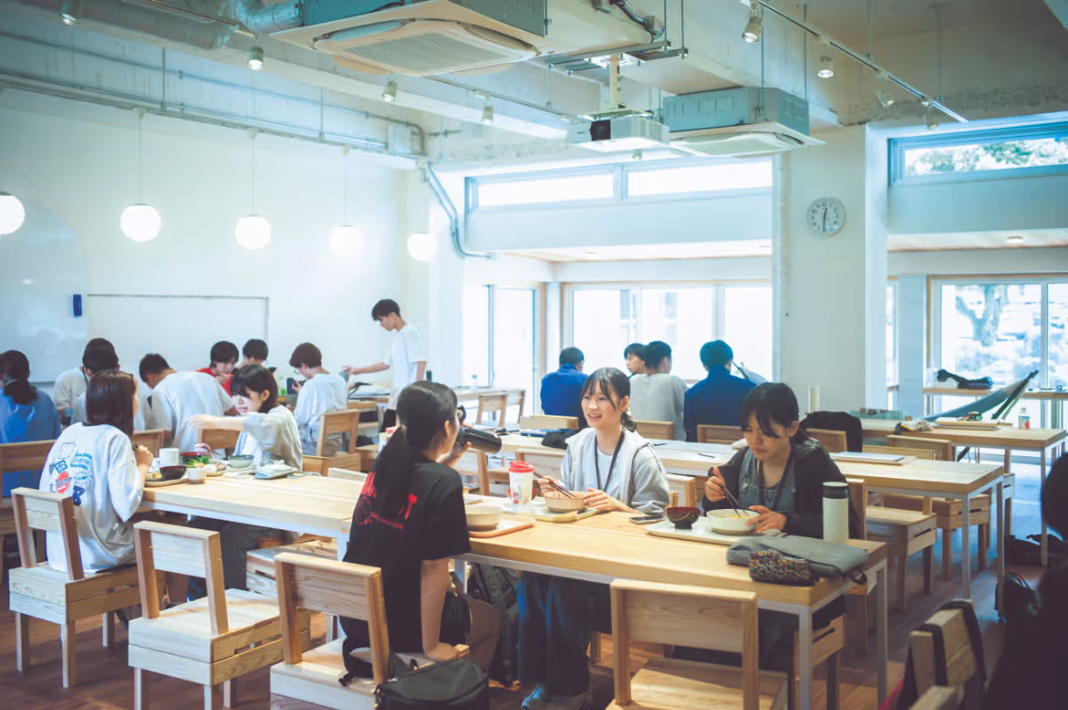 Students chat and eat in a cafeteria lined with wooden tables.